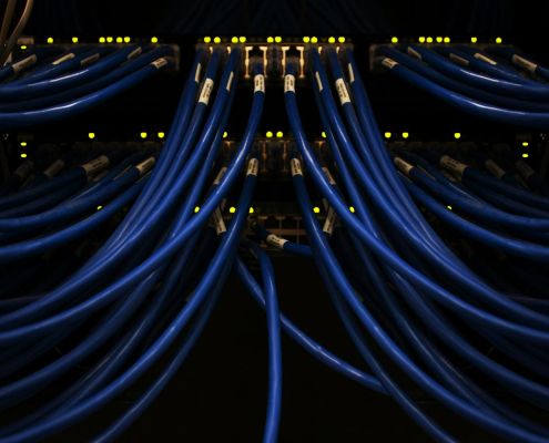 Close-up of blue Ethernet cables plugged into a network switch, with indicator lights glowing, inside a data center server rack.